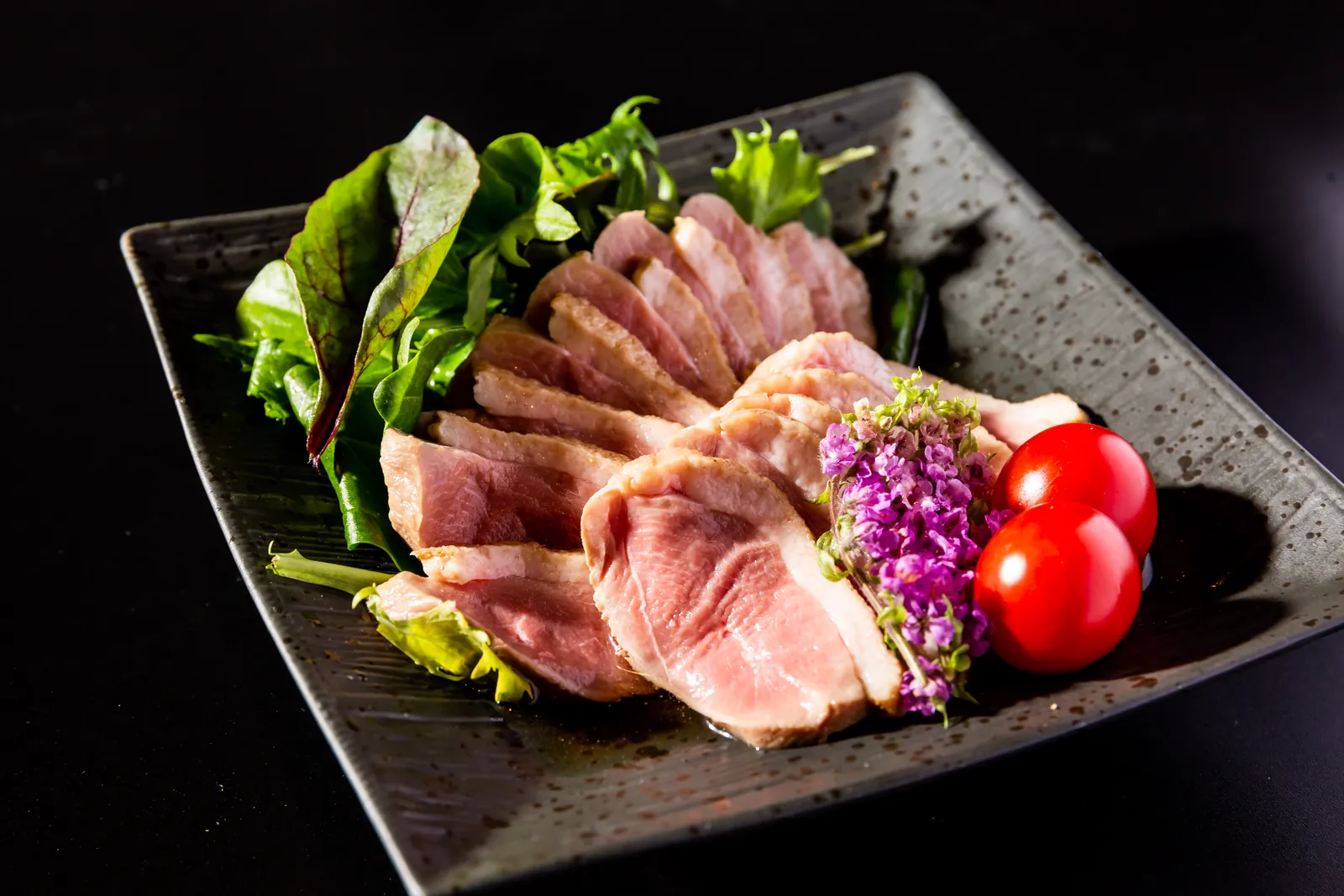 黒い器に盛り付けた肉料理と彩りある野菜